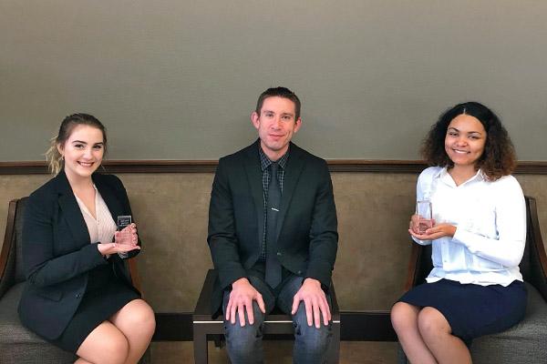 Three political science students sitting in courthouse lobby holding up awards